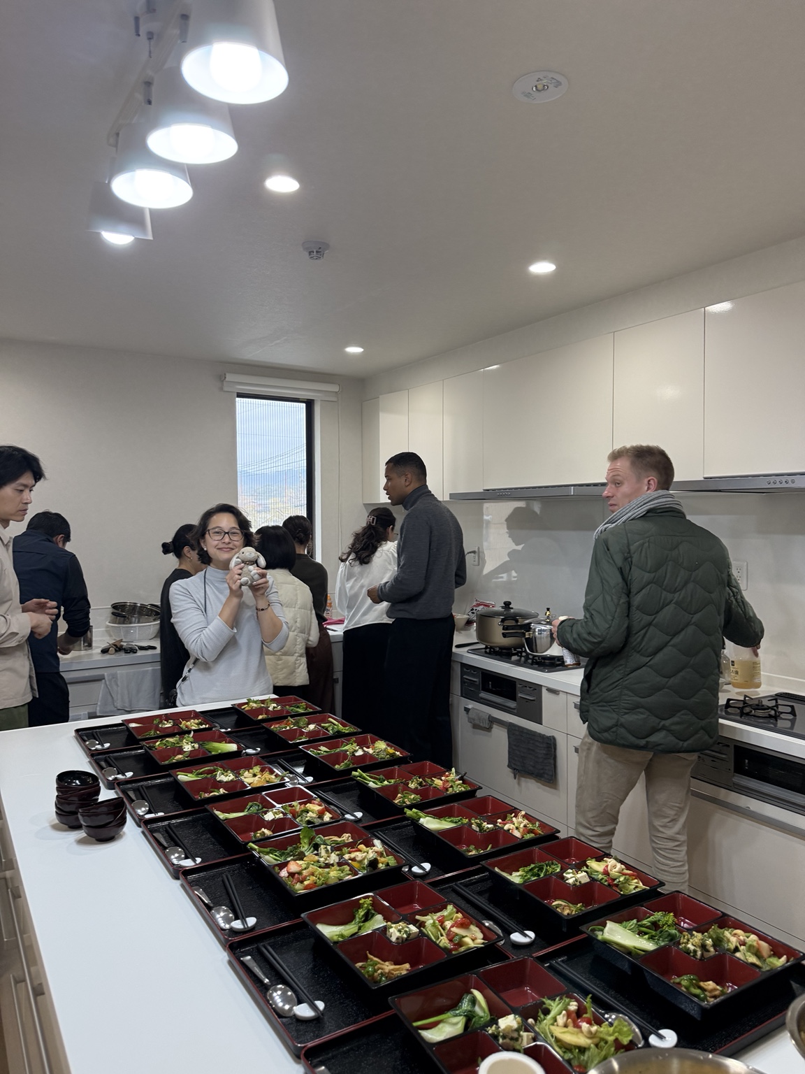 Rows of lacquered bento trays with freshly prepared plant-based dishes laid out on the kitchen counter before a shared meal.