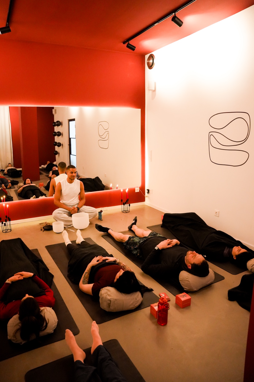 Participants lying on mats under blankets during a candlelit sound bath, with Nathan seated beside crystal singing bowls in the red-toned aōma studio.