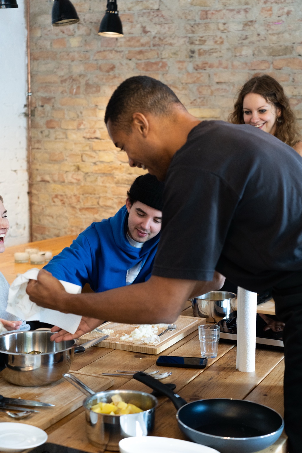 Participants laughing together around a wooden kitchen table with pots, pans and chopped onions during the mindful cooking workshop.