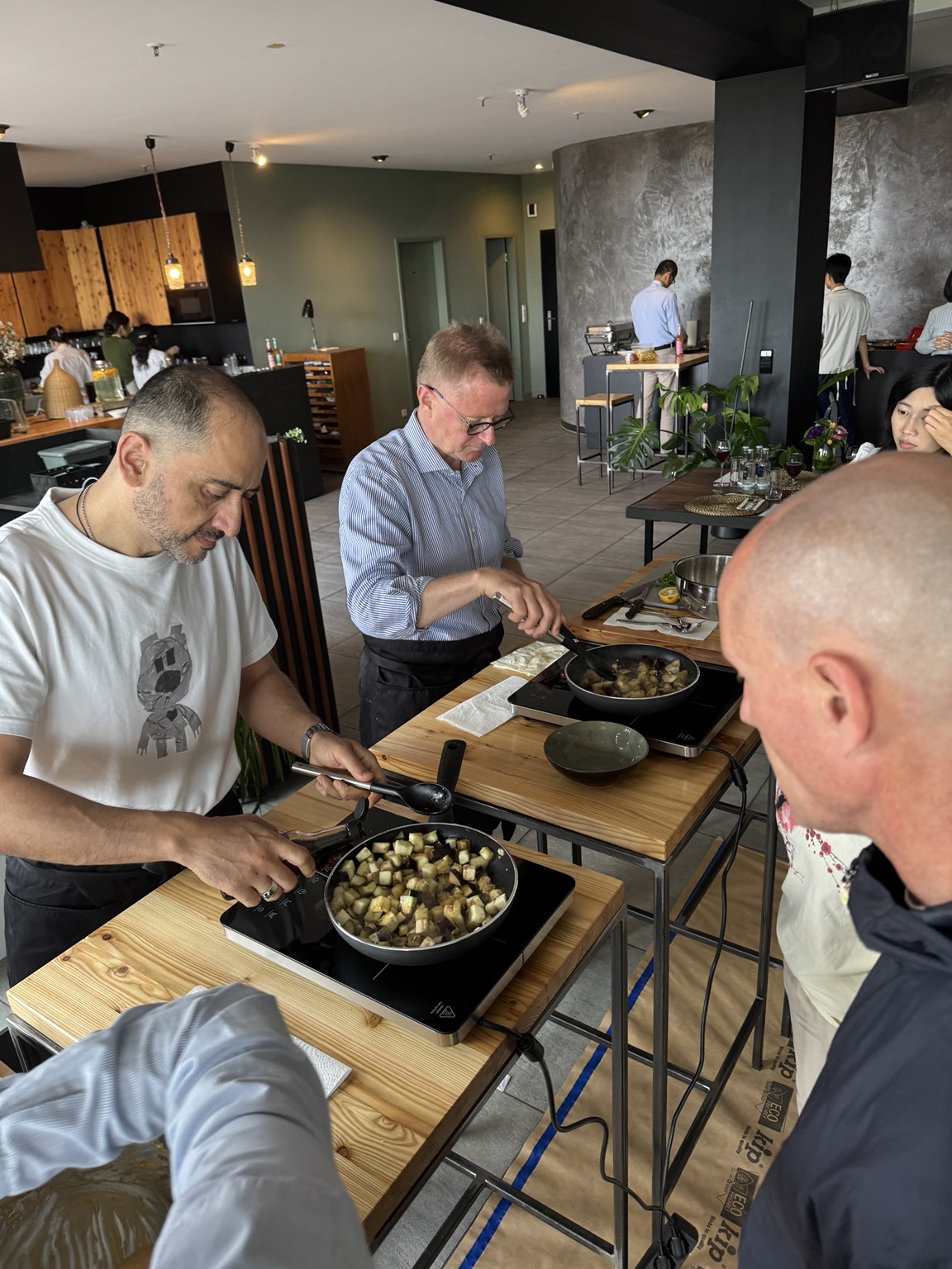 MDH team members in aprons frying diced aubergine at induction stations during the plant-based cooking workshop.
