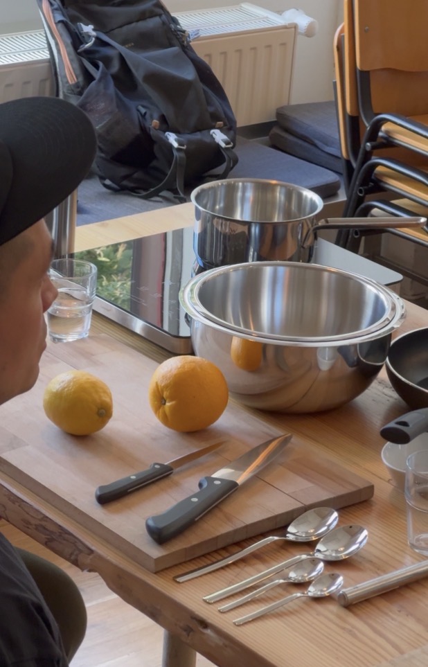 Lemons, an orange, knives, spoons and steel bowls laid out on a wooden table before a mindful cooking session.