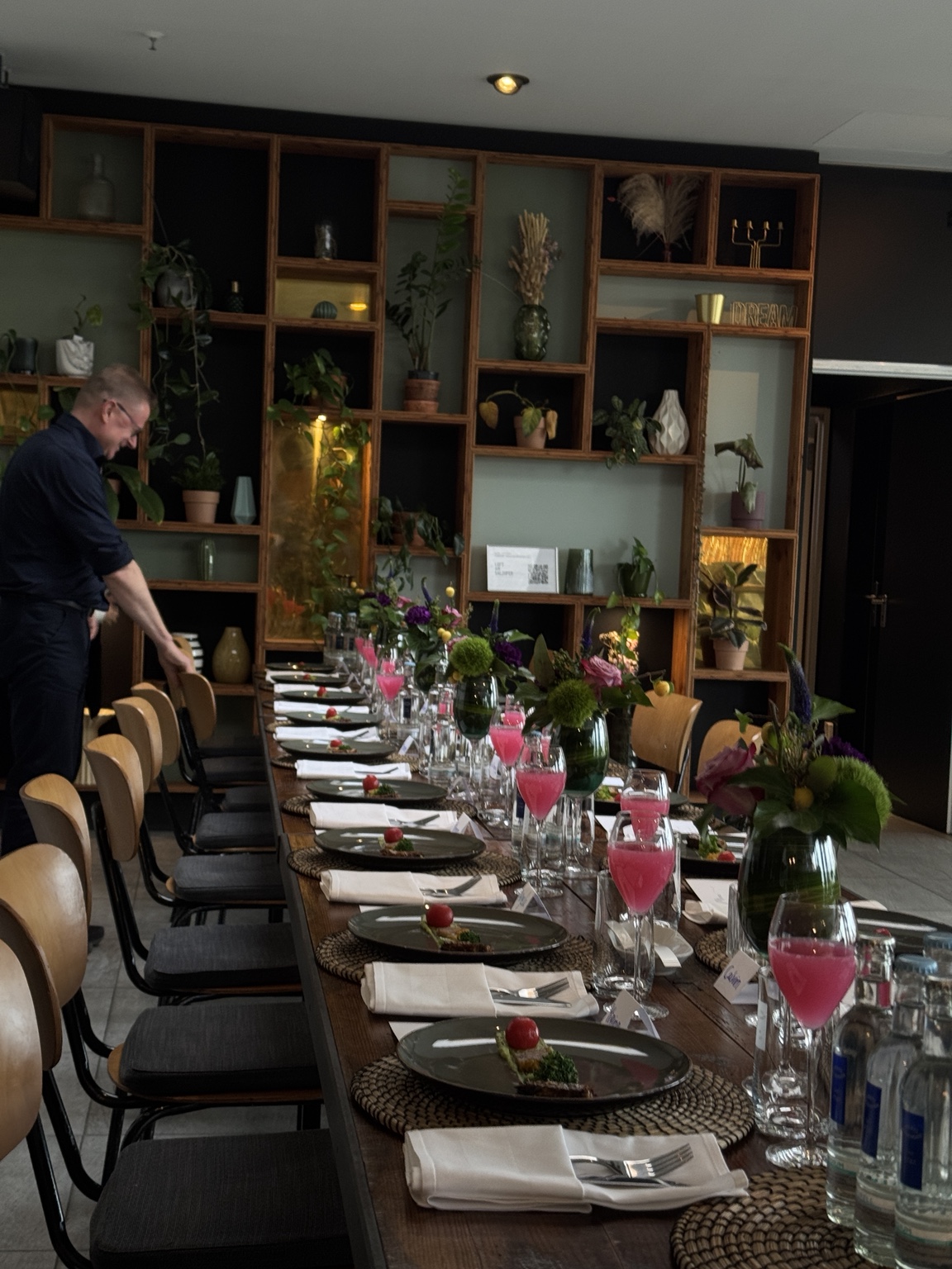 The long shared table laid with plated dishes, seasonal flowers and drinks before the group meal.