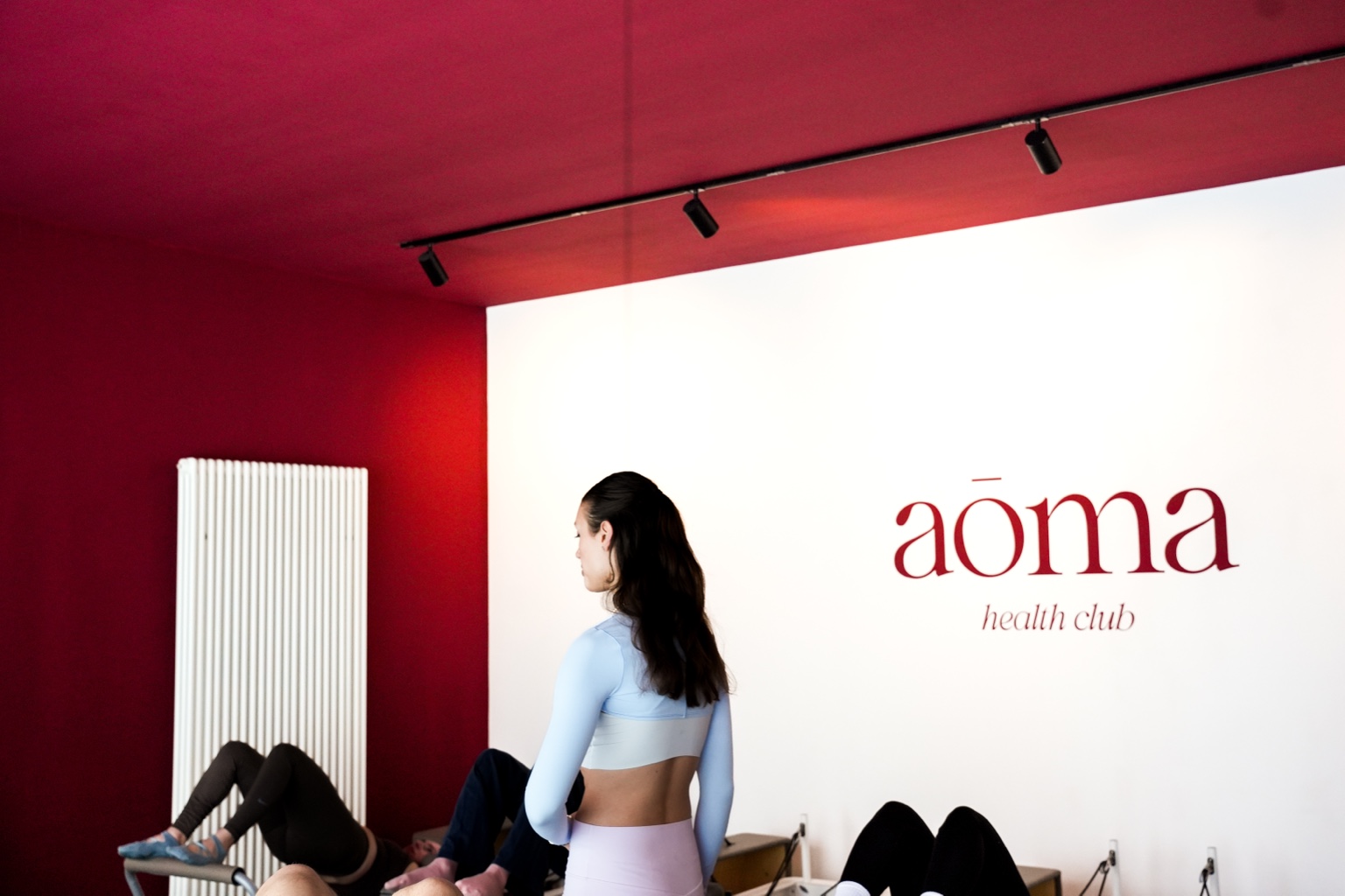 Katharina guiding the reformer session in front of the aōma health club wordmark painted on the studio wall.