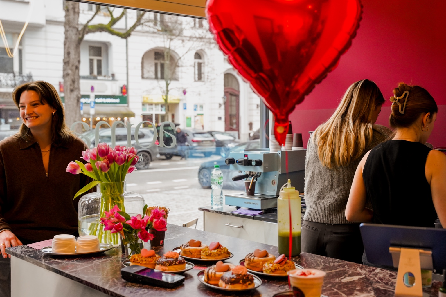 The welcoming café area at aōma with tulips, doughnuts, a coffee machine and a red heart balloon by the street-facing window.