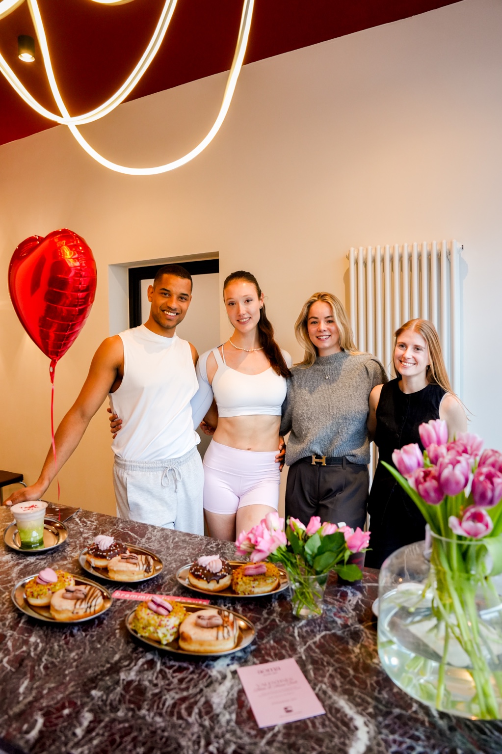 The four-person event team standing together behind the marble counter with a red heart balloon, pink tulips and plates of doughnuts.