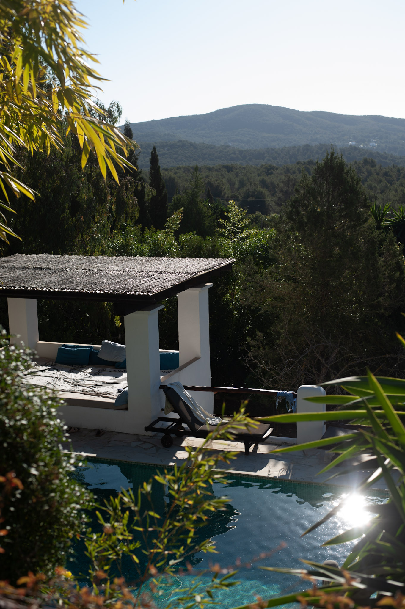 The retreat villa's shaded daybed pergola above the pool, with wooded hills of Ibiza in the distance.