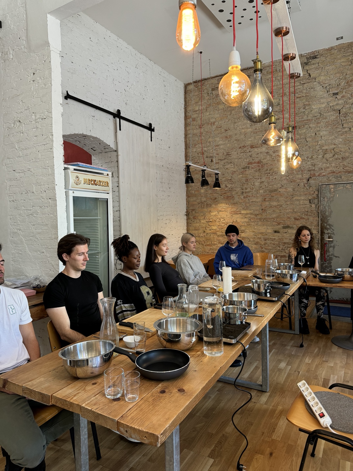 Participants seated with eyes closed for a short guided meditation at the long wooden cooking table before the workshop begins.
