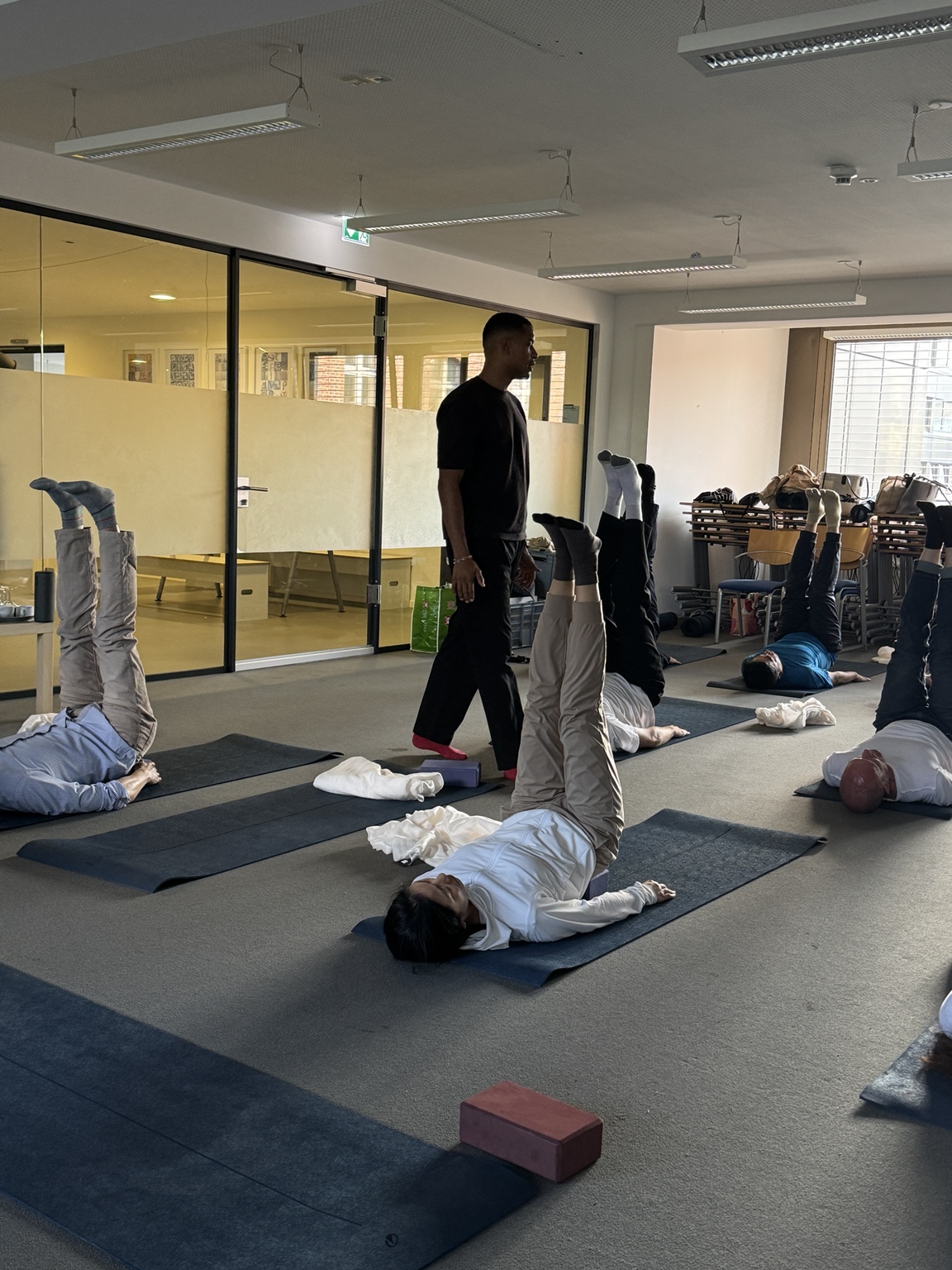 Participants in a shoulderstand on mats during the yoga session, with Nathan walking between them in the campus studio.