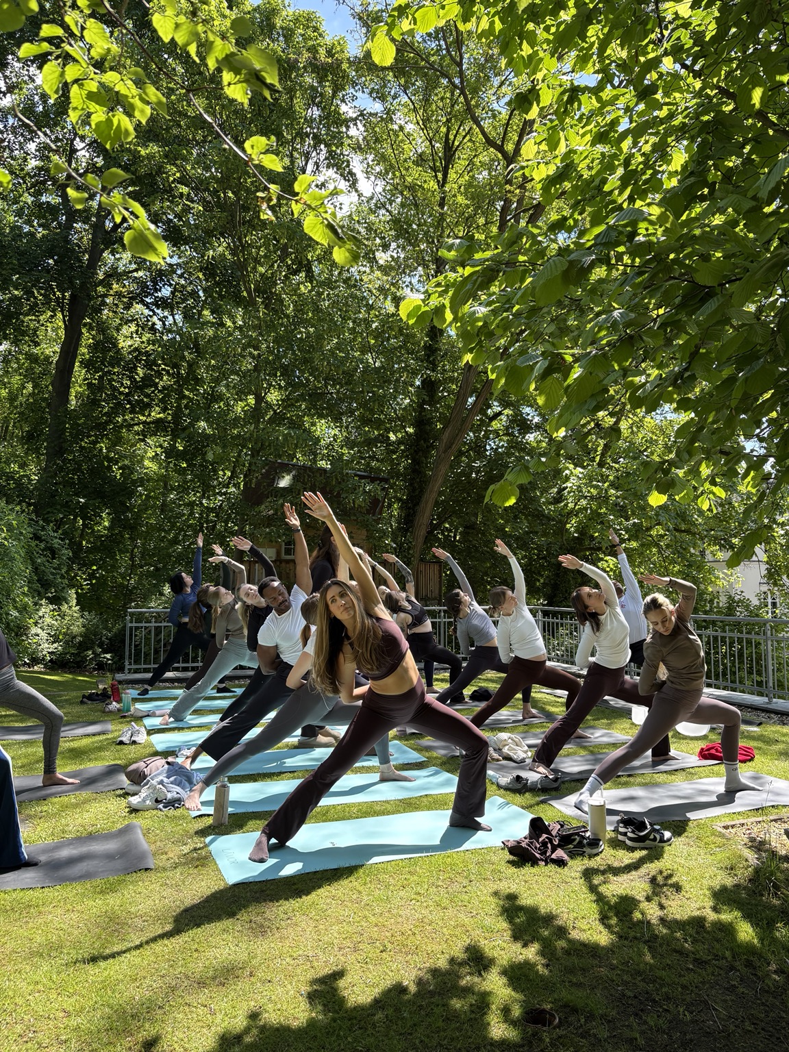 Participants in an extended side-angle pose on mats during outdoor yoga in a leafy Berlin garden.