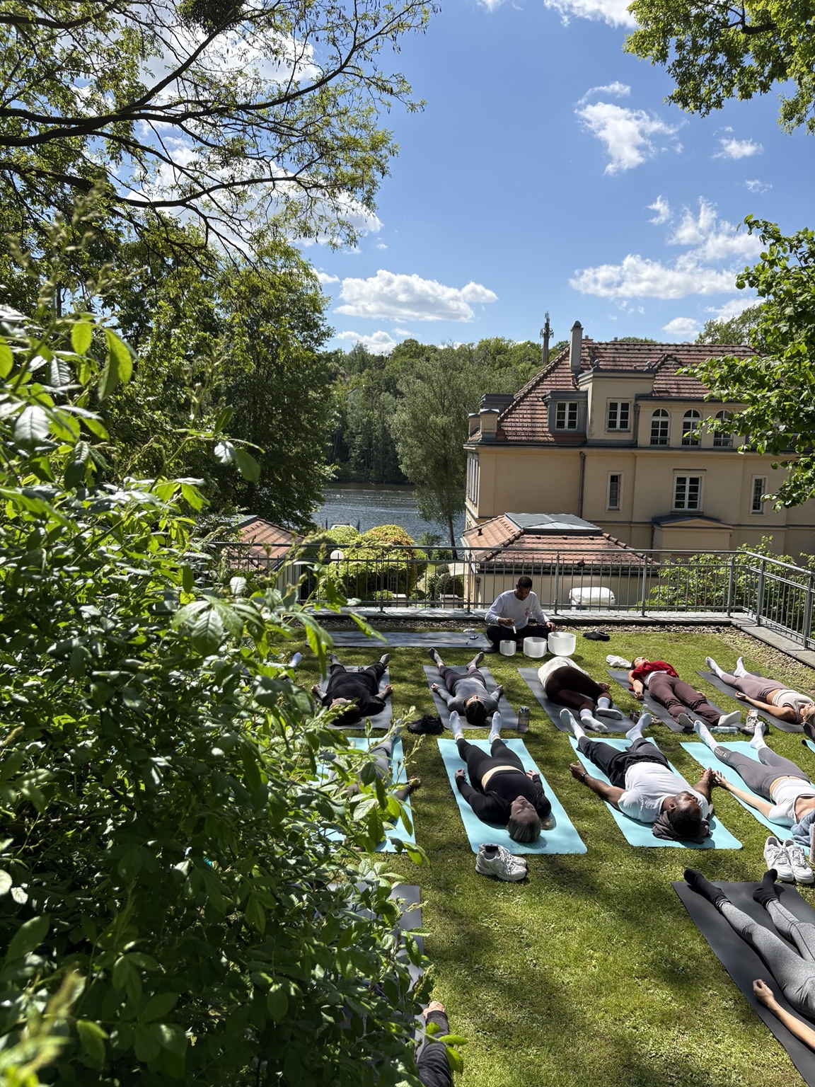Participants lying on mats for a sound bath led by Nathan with crystal bowls, overlooking a lake and villa in Berlin.