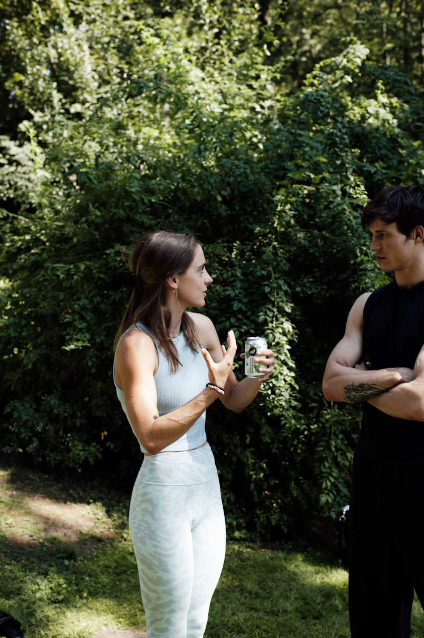 Two participants in conversation with drinks in hand in front of dense green foliage after the practice.
